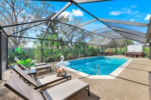 Piscina al aire libre con sillones de descanso y un flotador con forma de cisne, rodeada por un área techada con vista a árboles.
