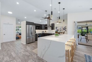 A modern kitchen with a large island, stainless steel appliances, and pendant lighting. - North Naples oasis near Mercato and beaches with screened private pool & hot tub (Naples)