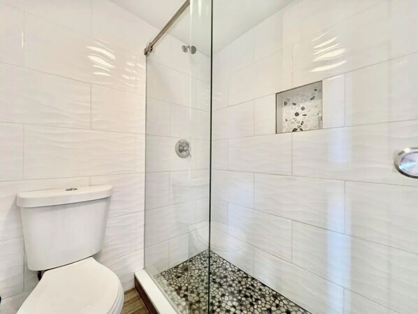 A modern bathroom with a glass shower enclosure, white tiled walls, and a mosaic tile floor.