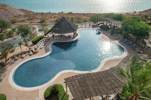 A large, curved swimming pool with a thatched-roof pavilion and lounge chairs.