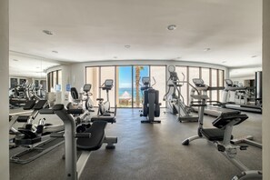 A gym with various exercise machines, large windows, and a view of the ocean.