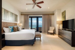 Ein Hotelzimmer mit Bett, Fernseher, Deckenventilator, Meerblick und einem Balkon.