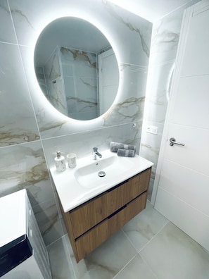 Een badkamer met een marmeren wastafel, een ronde spiegel, een wastafel en een toilet.