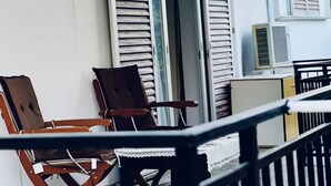 Een balkon met houten stoelen en een kleine tafel, een witte airconditioning en een witte balustrade.