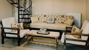 Ein Wohnzimmer mit Wendeltreppe, einer Sofagarnitur, zwei Sesseln, einem Couchtisch und einer Pendelleuchte.