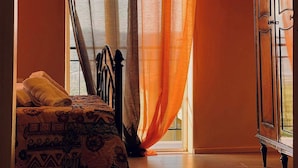 Ein Schlafzimmer mit Bett, Kleiderschrank und durchsichtigen Vorhängen.