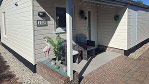 A single-story house with a number '132' on the door, a porch with a bench, and a flamingo statue.
