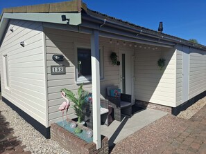 A single-story house with a number '132' on the door, a porch with a bench, and a flamingo statue.