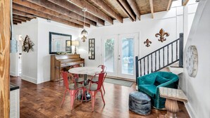 A spacious room with a wooden ceiling, a piano, a round table with chairs, and a staircase with a railing.
