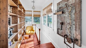 A hallway with wooden shelves, a yellow armchair, and a large wall clock.