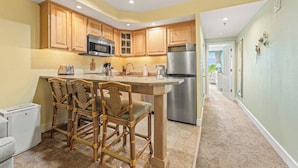 A kitchen with wooden cabinets, a stainless steel refrigerator, and a bar area with wicker chairs.
