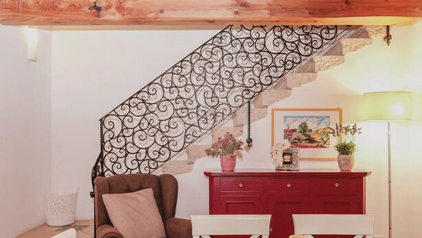 A cozy living room with a brown sofa, white chairs, a red cabinet, and a staircase with a decorative railing. - Borgo degli Angeli Resort & Spa (Partinico)