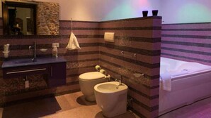 A bathroom with a stone accent wall, a bathtub, a toilet, and a sink. - Luxury Suite Wellness & Resort (Partinico)