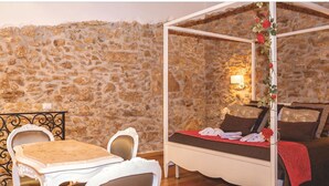 A room with a stone wall, a bed with a canopy, a table with chairs, and a small table with a chair. - Luxury Suite Wellness & Resort (Partinico)