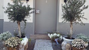 A building entrance with a grey door, two potted trees, and a small garden area with flowers and a checkered mat. - French country house on the Rhine, large courtyard, parking spaces, pet-friendly (Trebur)