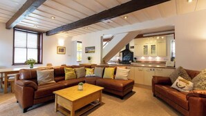 A cozy living room with a brown leather sofa set, a wooden coffee table, and a staircase leading to a kitchen area.