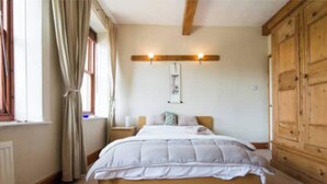A bedroom with a wooden bed, a nightstand, a wooden wardrobe, and a window with curtains.