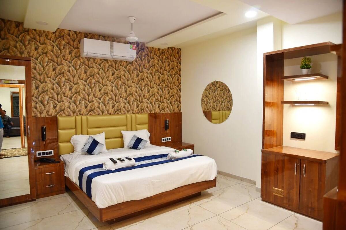 A hotel room with a large bed, wooden headboard, a mirror, a wardrobe, and a wall with a textured pattern.