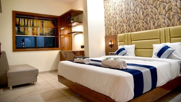 Ein Hotelzimmer mit einem großen Bett, einer kleinen Sitzecke, einem Bild an der Wand und einer strukturierten Wand hinter dem Bett.