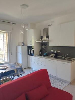 Une cuisine moderne avec des meubles blancs, une cuisinière à gaz, un évier et un coin repas comprenant une chaise et une table rouges.