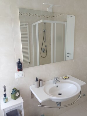 Een badkamer met een wit wastafel, een spiegel, een douche en een toilet.