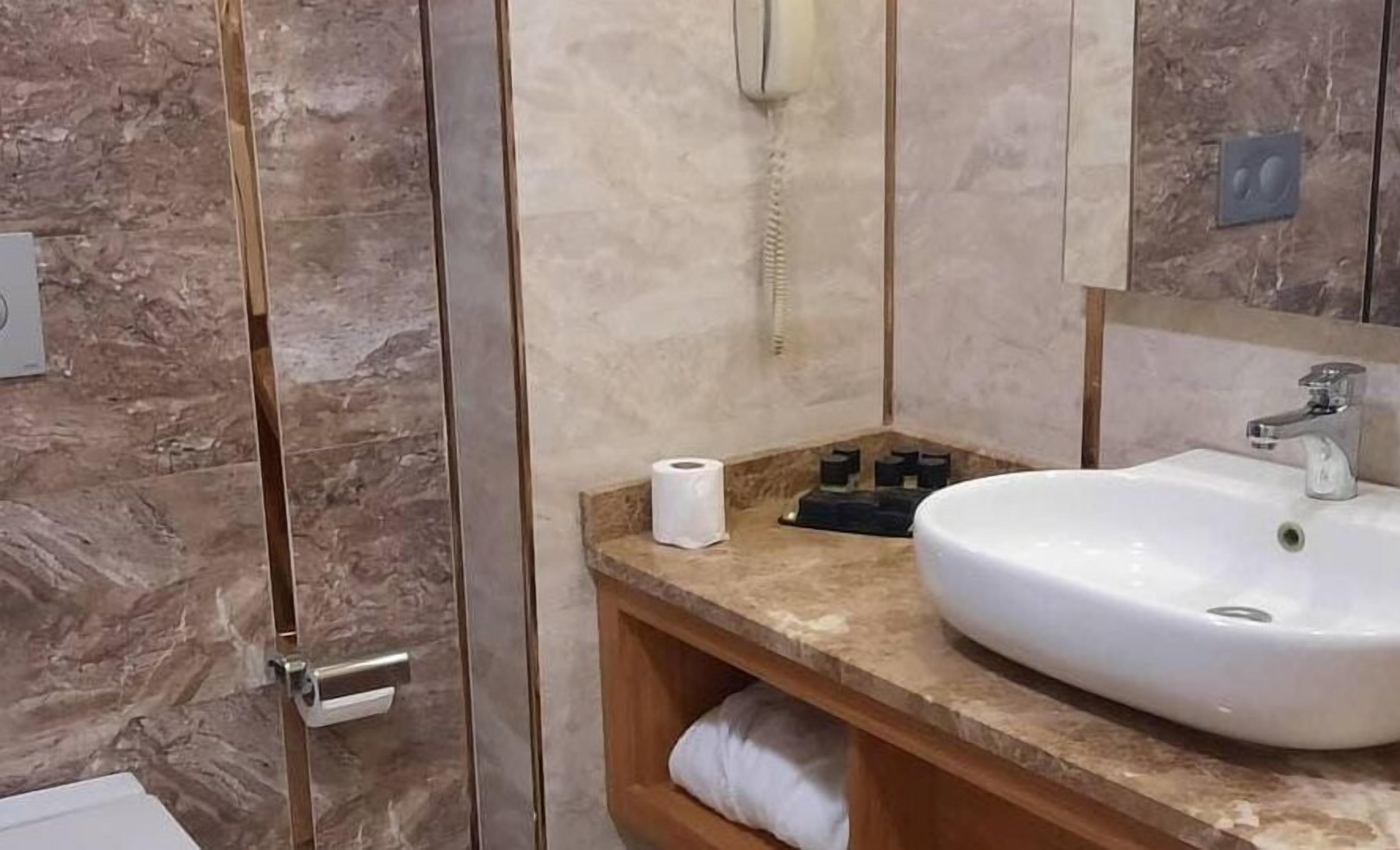 A bathroom with a marble wall, a white sink, a mirror, and a towel rack.