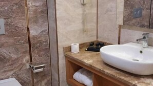 Un baño con pared de mármol, lavamanos blanco, espejo y toallero.