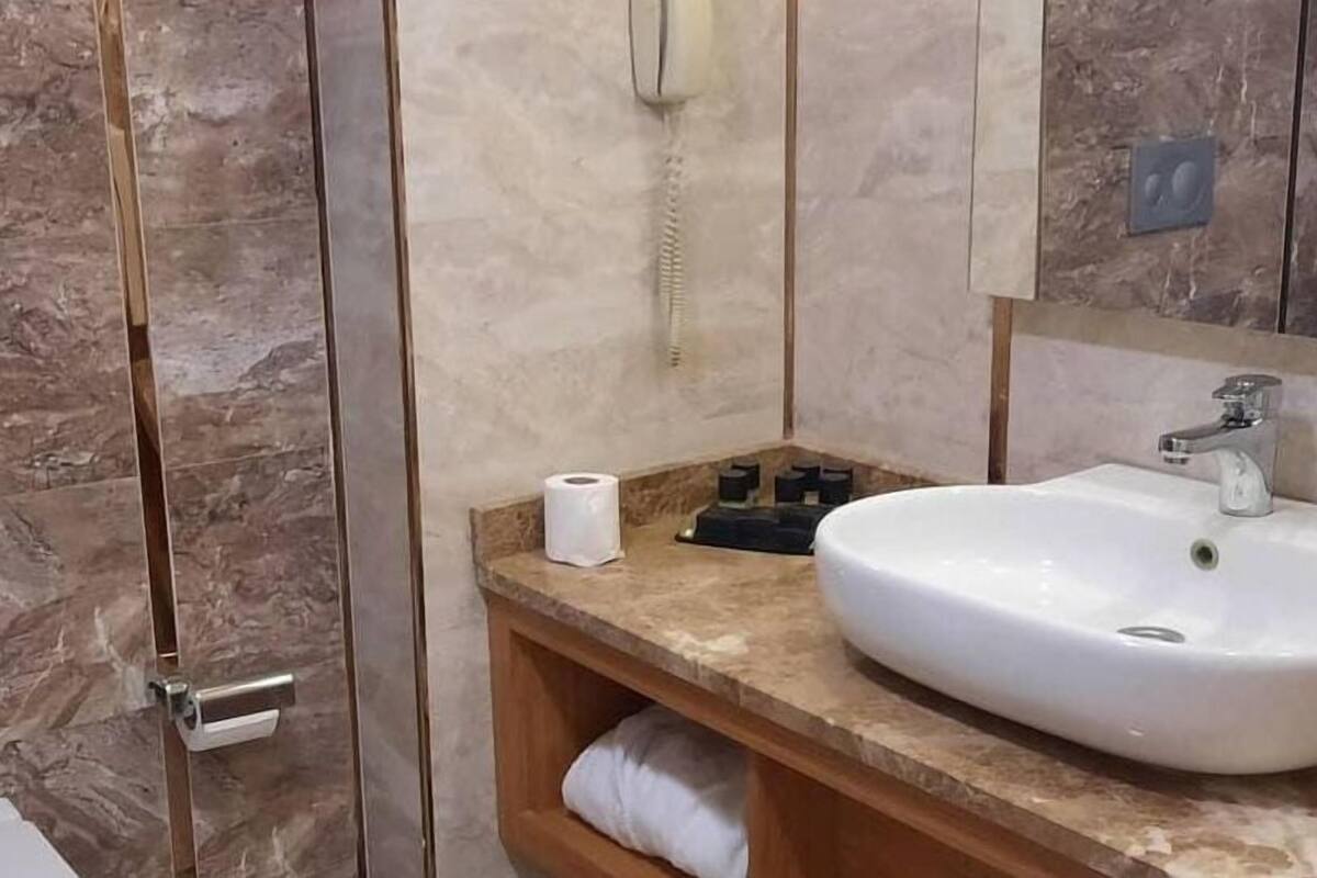 A bathroom with a marble wall, a white sink, a mirror, and a towel rack.