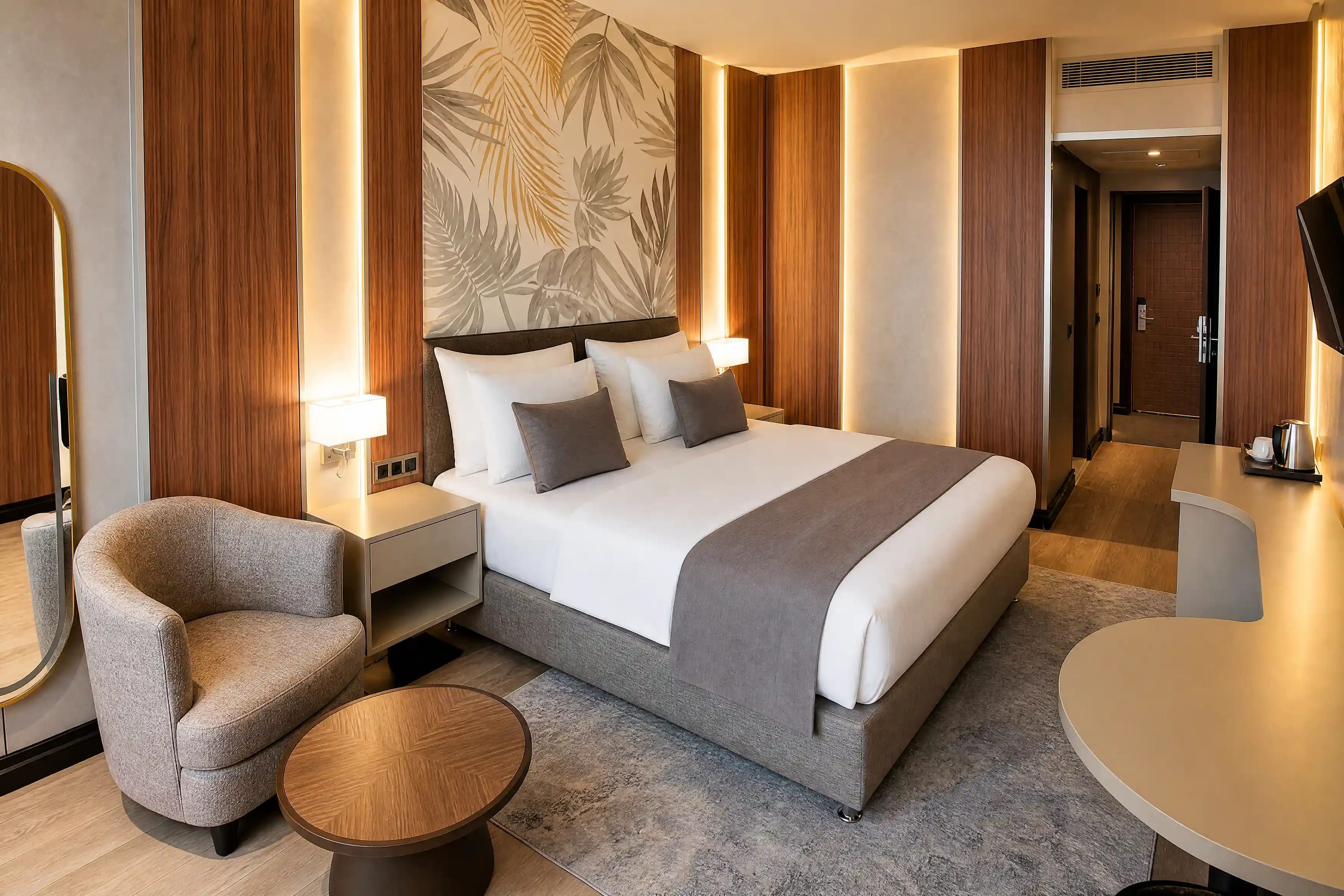 A hotel room with a bed, bedside tables, a chair, a round table, and a wall with a leaf pattern.