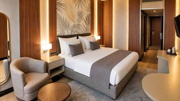 A hotel room with a bed, bedside tables, a chair, a round table, and a wall with a leaf pattern.