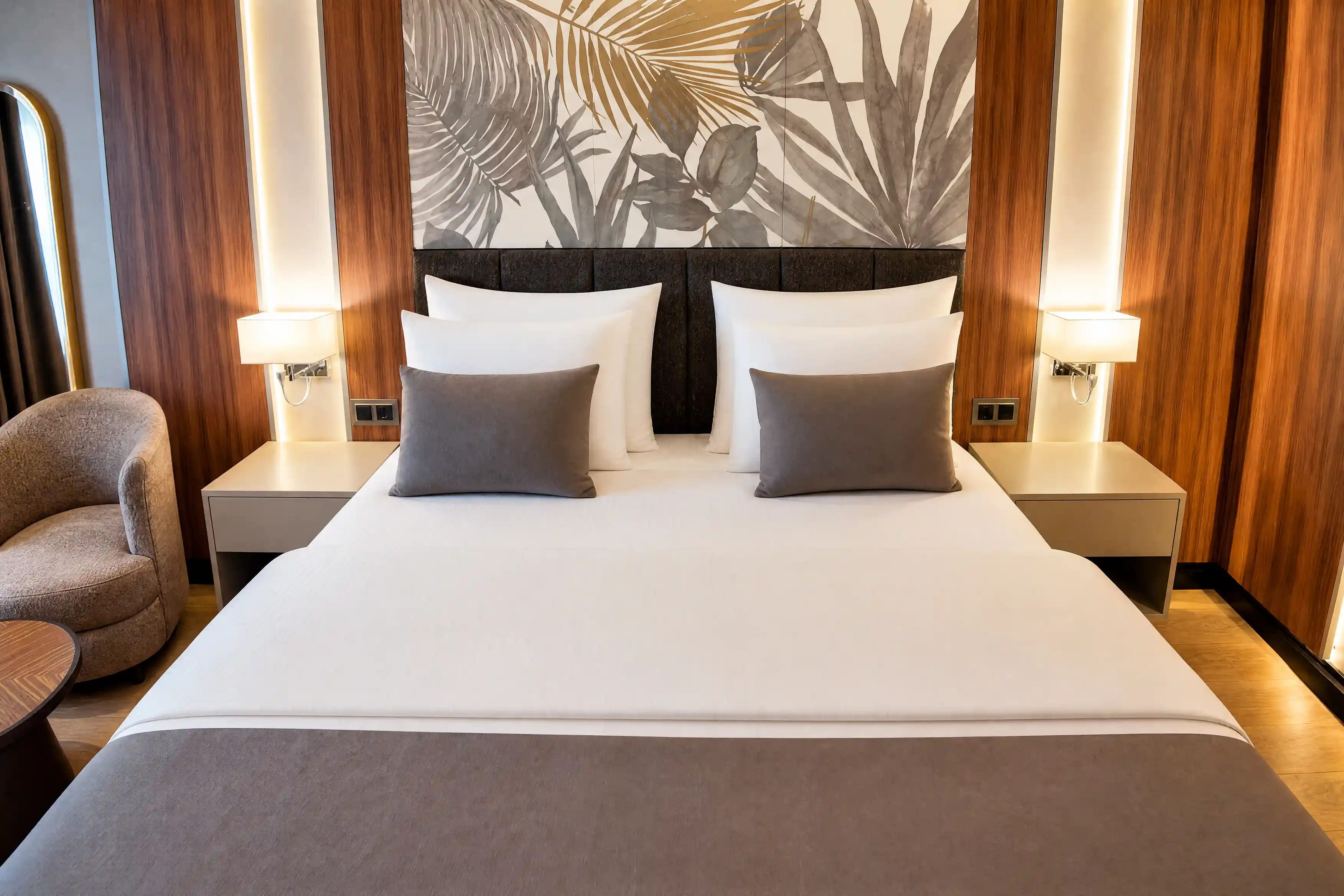 Ein Hotelzimmer mit einem großen Bett, zwei Nachttischen, einem Sessel und einer Wand mit einem Blattmuster.