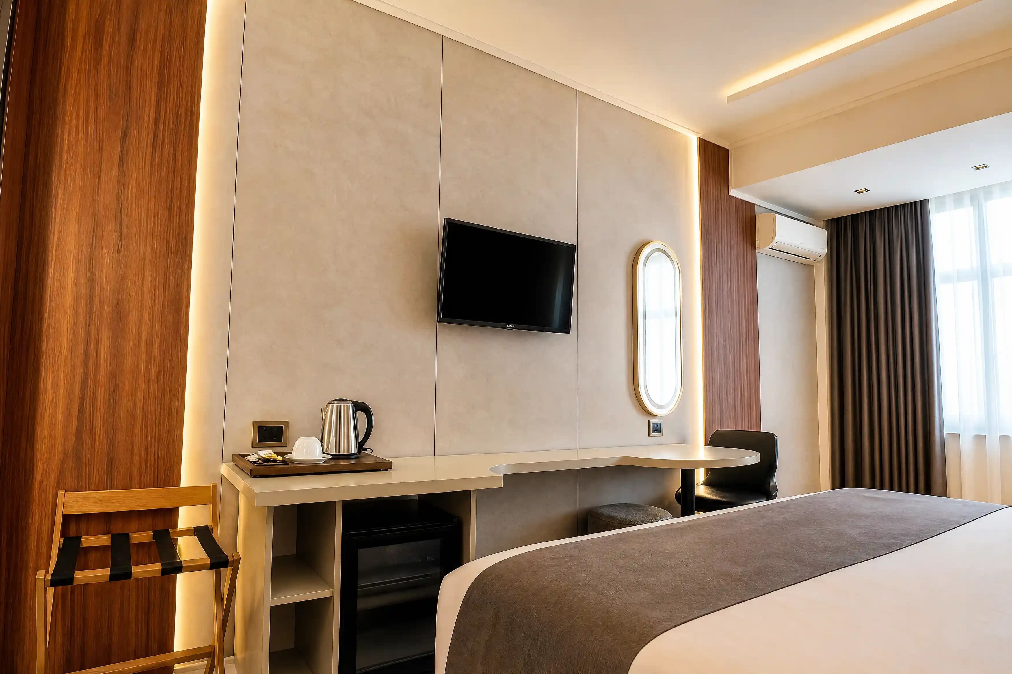 A hotel room with a bed, a desk with a flat-screen TV, a coffee maker, a mirror, and a window with curtains.