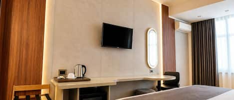 A hotel room with a bed, a desk with a flat-screen TV, a coffee maker, a mirror, and a window with curtains.