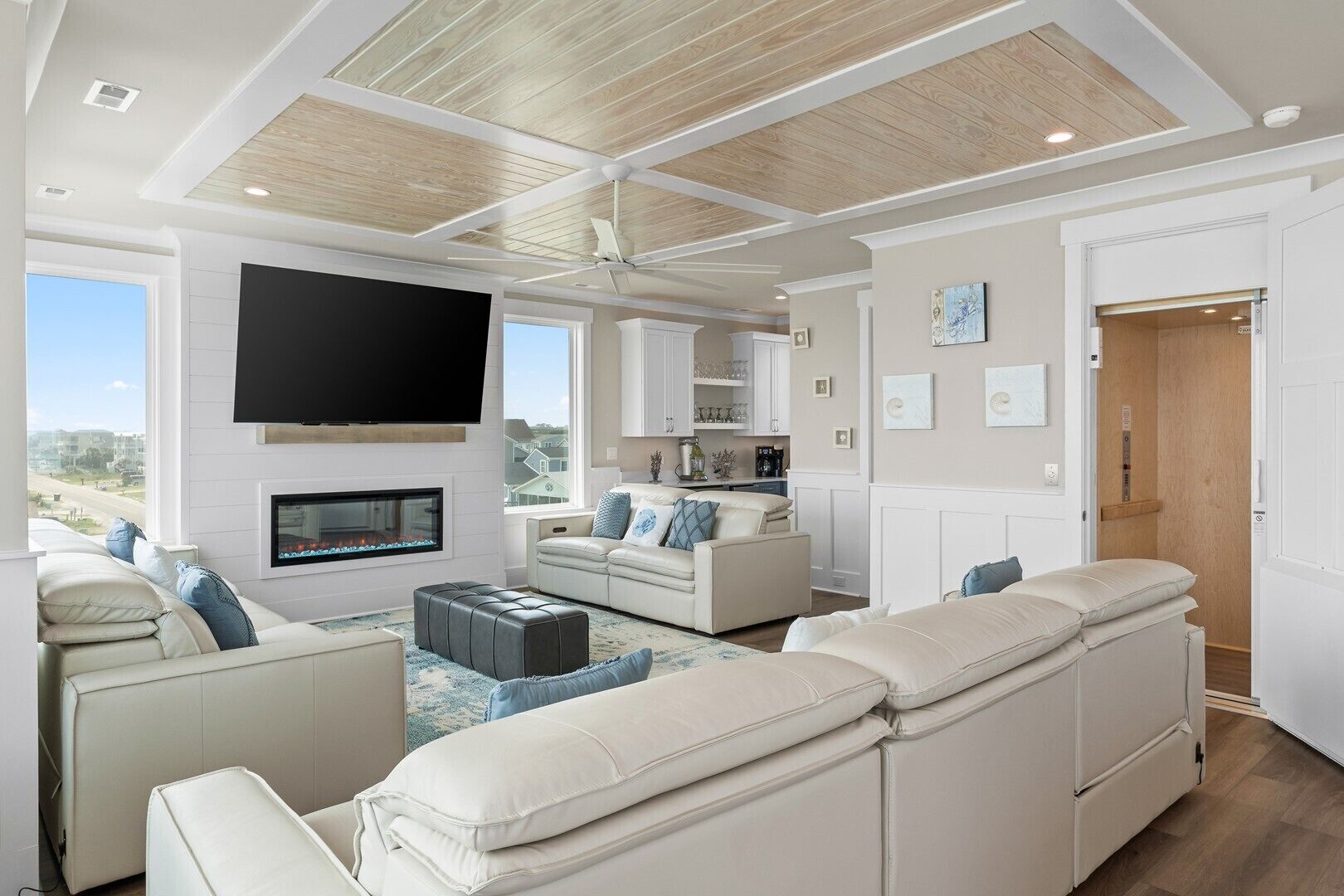 A spacious living room with a fireplace, a flat-screen TV, and a large window offering a view of the outdoors.