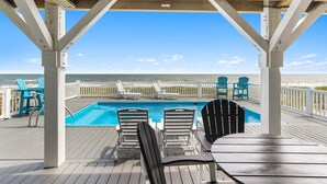 A wooden deck with a pool, lounge chairs, and a view of the ocean.
