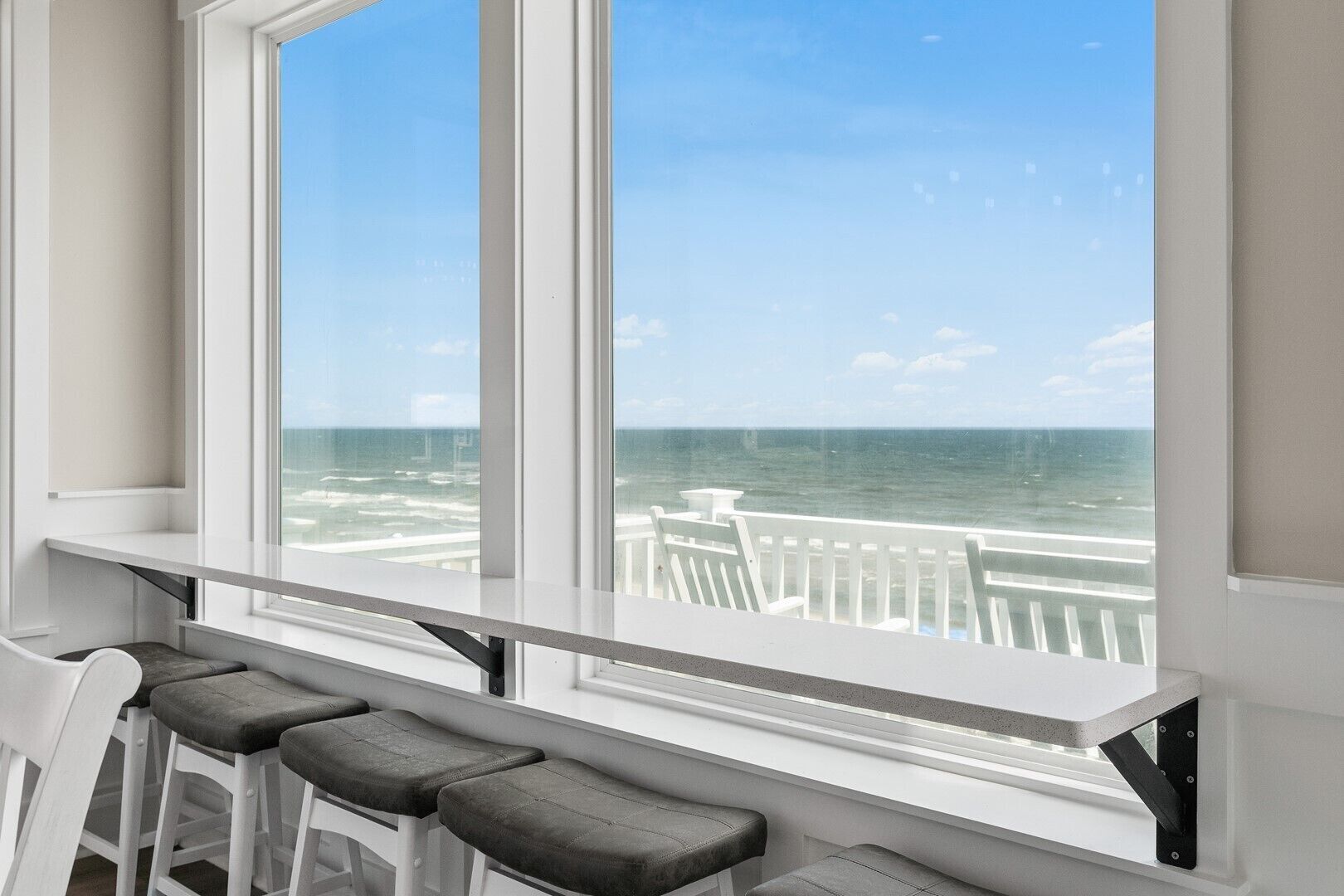Ein Zimmer mit großem Fenster und Meerblick, eine weiße Bank und ein weißer Geländer.