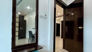 A hallway with a large mirror, a teal ottoman, and a dark wooden door.