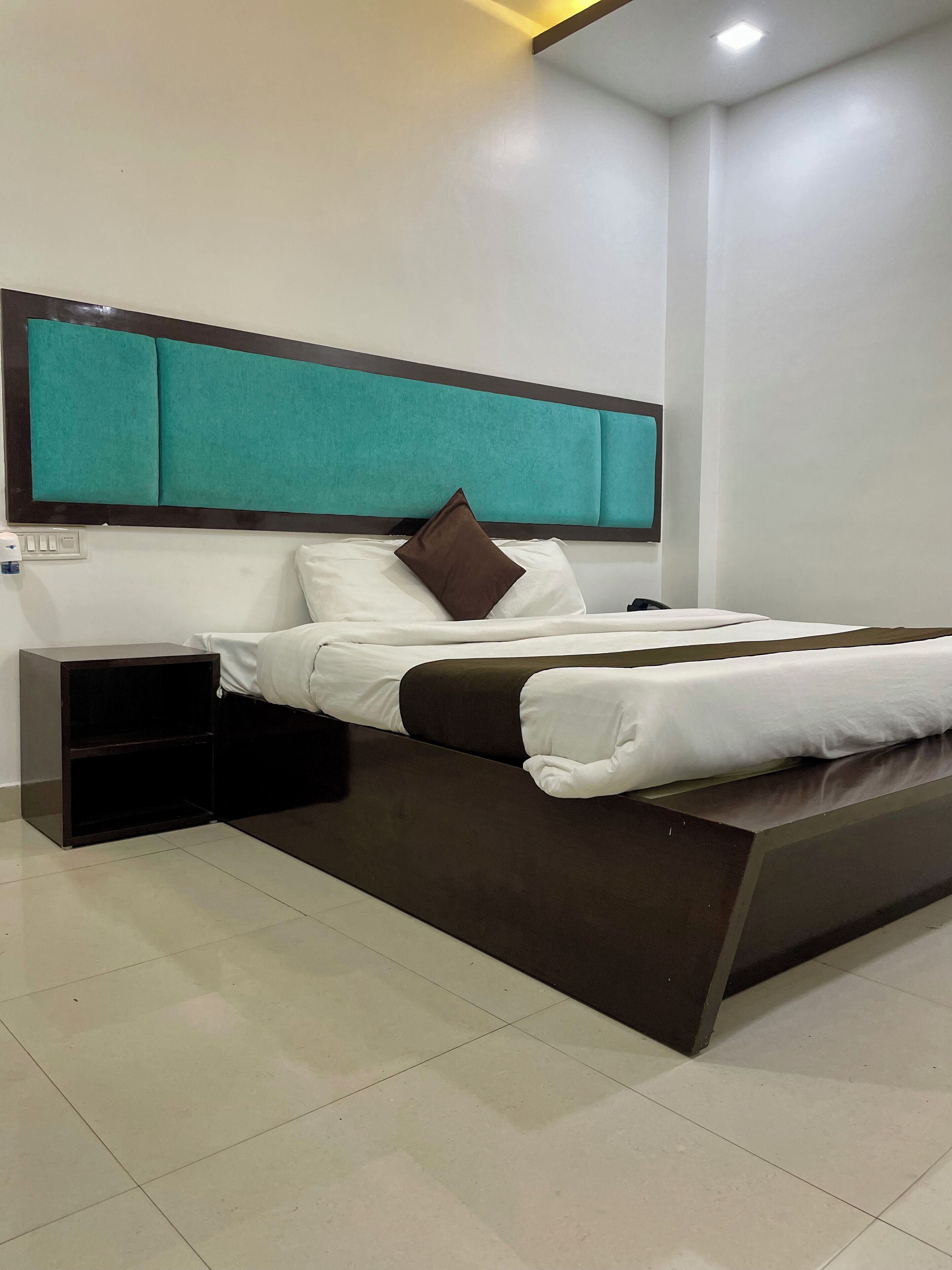 A modern hotel room with a large bed, a nightstand, and a built-in bench.