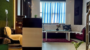A modern living room with a reception desk, a sofa, a chair, and a potted plant.