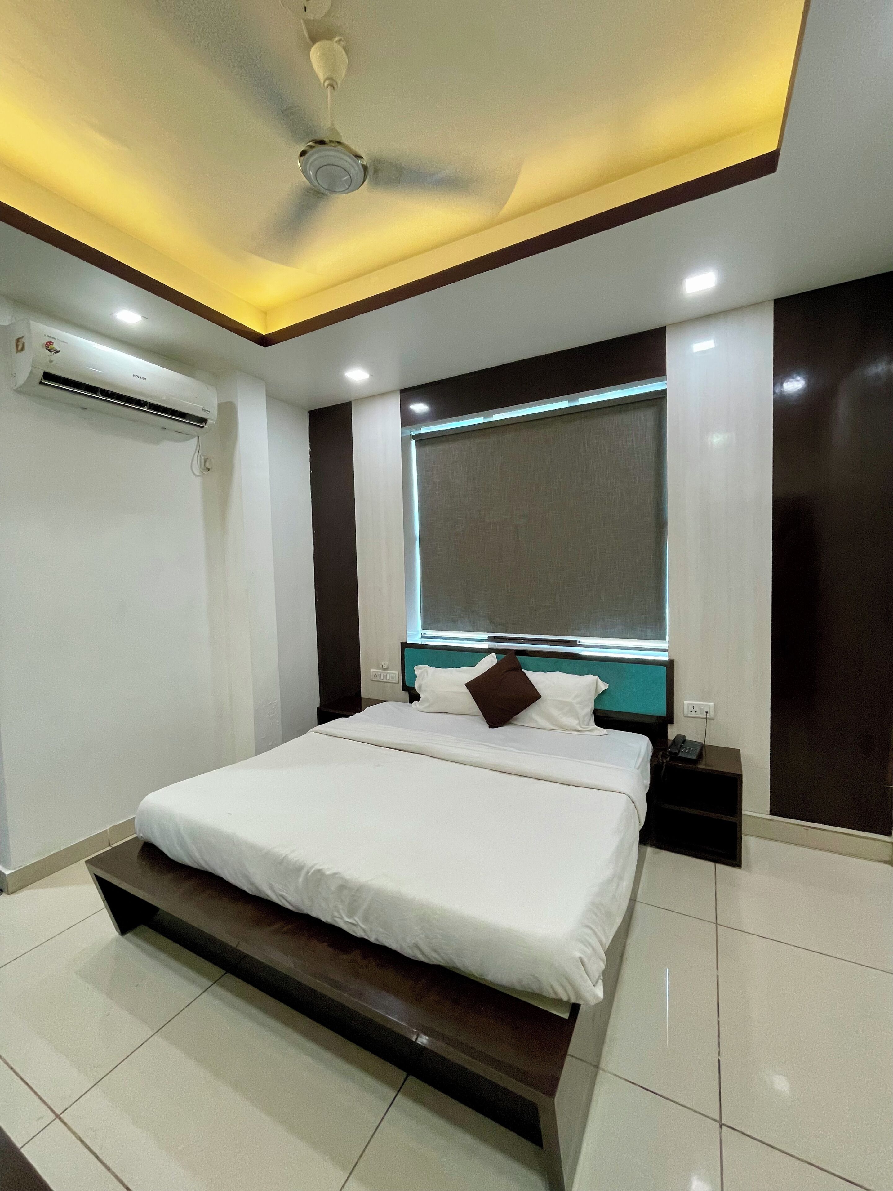 A modern hotel room with a bed, a nightstand, an air conditioning unit, and a ceiling fan.