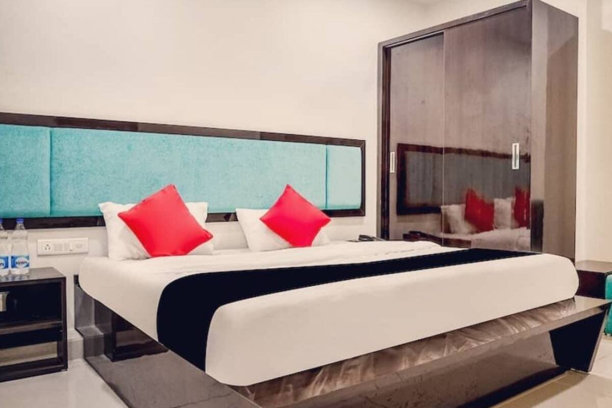 A modern hotel room with a large bed, a nightstand, a mirror, and a teal armchair.
