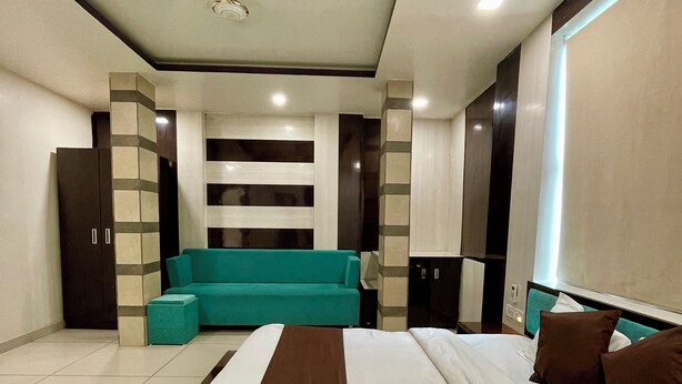 A modern hotel room with a large bed, a teal sofa, and a small table.