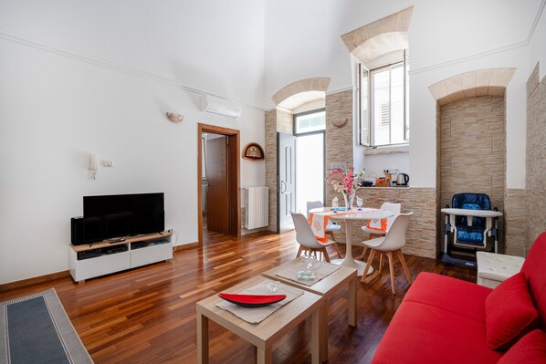Una sala de estar moderna con un televisor de pantalla plana, un comedor con mesa y sillas, un sofá rojo y un cambiador para bebés.