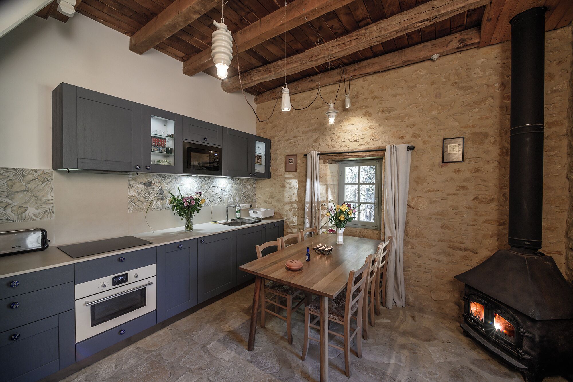 Una cocina rústica con paredes de piedra, una mesa de madera y un horno de leña.