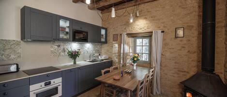 Una cocina rústica con paredes de piedra, una mesa de madera y un horno de leña.