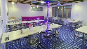 Un restaurante con piso de diseño azul, mesas y sillas blancas. Se observan ventiladores de techo e iluminación colgante.
