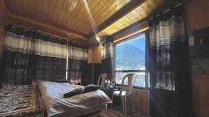 Habitación de cabaña de madera con una cama, una silla y una ventana con vistas a un paisaje montañoso.
