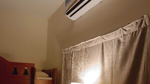 A room with a bunk bed, a standing lamp, a window with curtains, and an air conditioning unit.