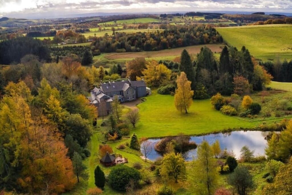 An aerial view of a rural property with a large house, a pond, and surrounding fields.