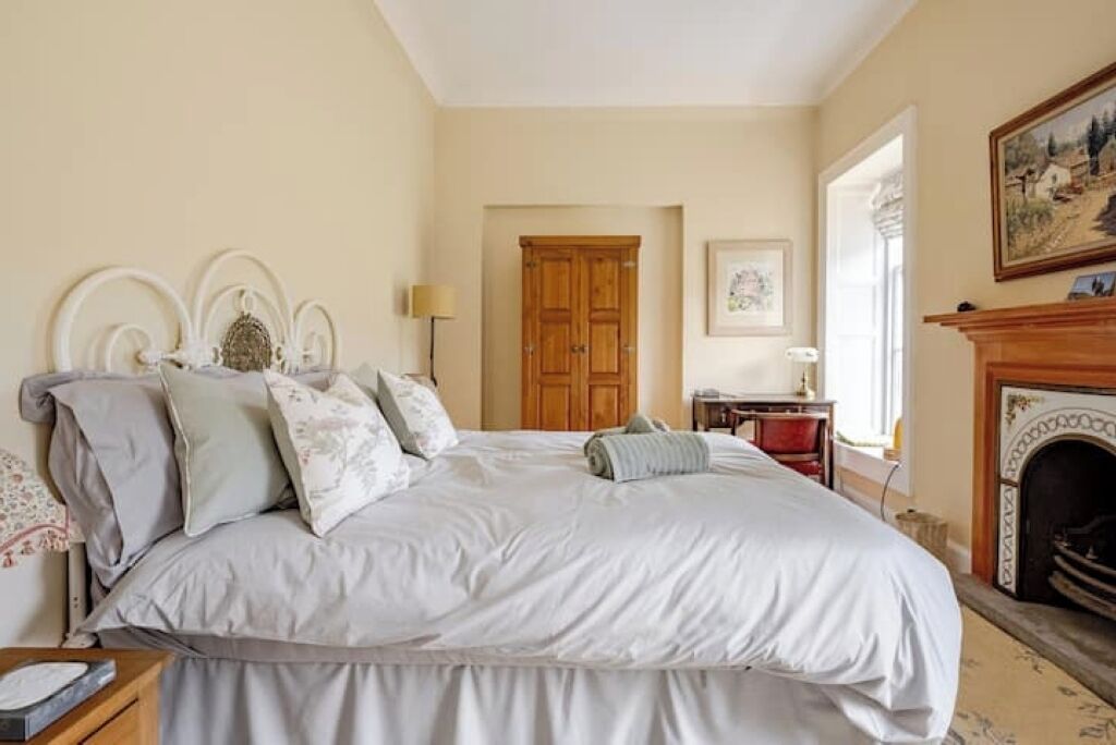 A bedroom with a large bed, a wooden wardrobe, a fireplace, and a framed picture on the wall.